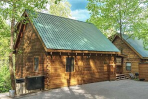 A wooden cabin with a sloped metal roof, a front porch, and a small attached structure.