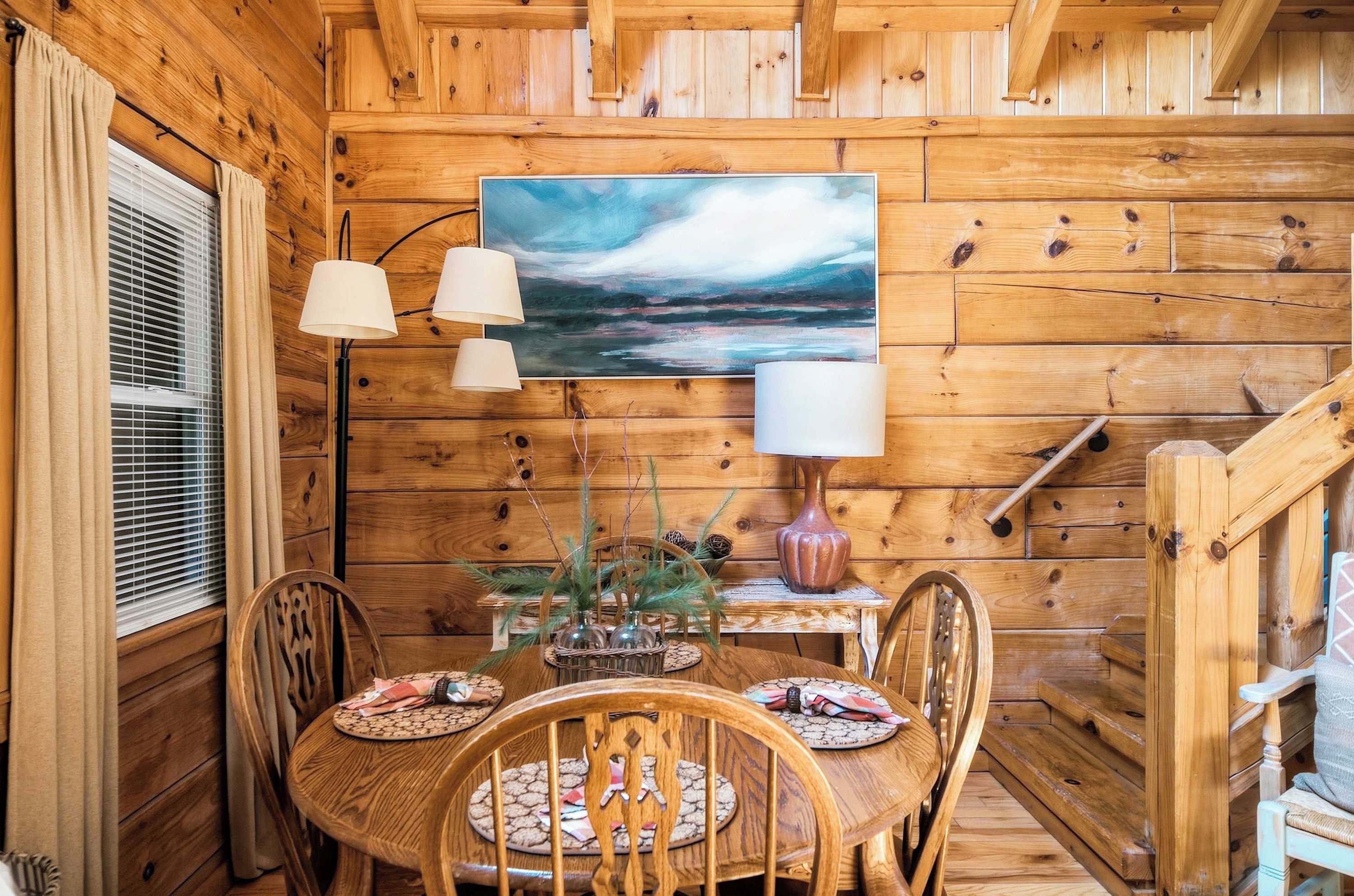 Un intérieur en bois avec une table ronde, des chaises, un tableau et une lampe.
