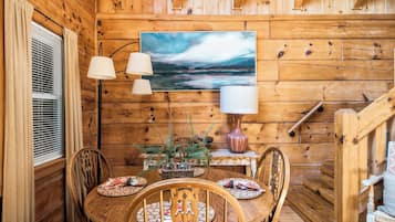 Un intérieur en bois avec une table ronde, des chaises, un tableau et une lampe.