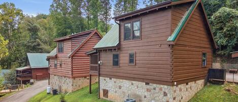 A log cabin with a stone foundation, a covered porch, and a small attached shed.
