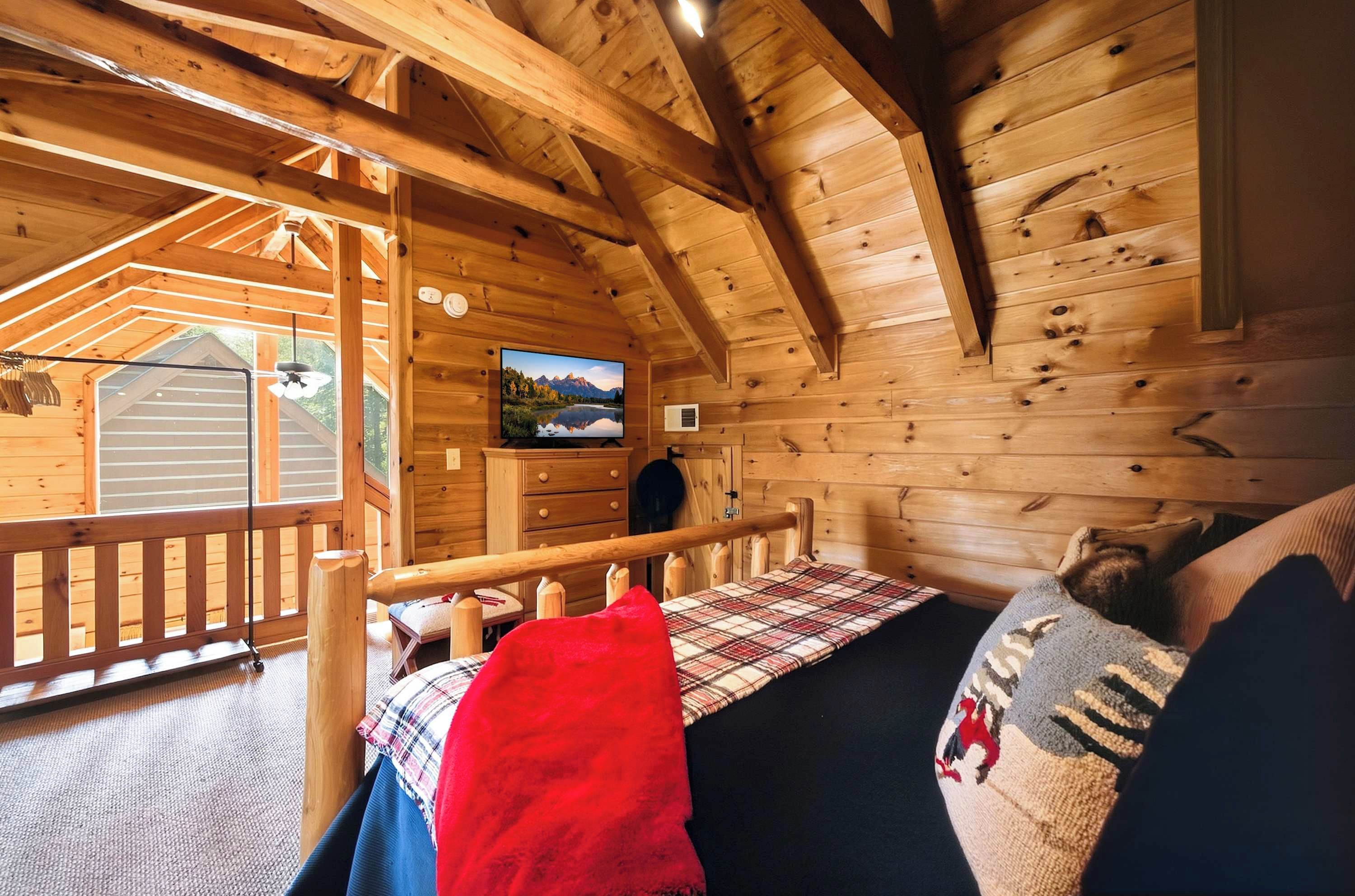 A cozy cabin interior with a bed, a television mounted on the wall, and a wooden deck outside.