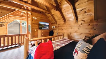 A cozy cabin interior with a bed, a television mounted on the wall, and a wooden deck outside.