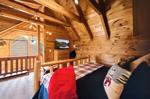 A cozy cabin interior with a bed, a television mounted on the wall, and a wooden deck outside. - Best Location - Cozy Log Cabin - Hot Tub & Pool (Gatlinburg)