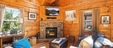 Interior acogedor de una cabaña con chimenea de piedra, paredes de madera y un ventanal con vistas a la vegetación.