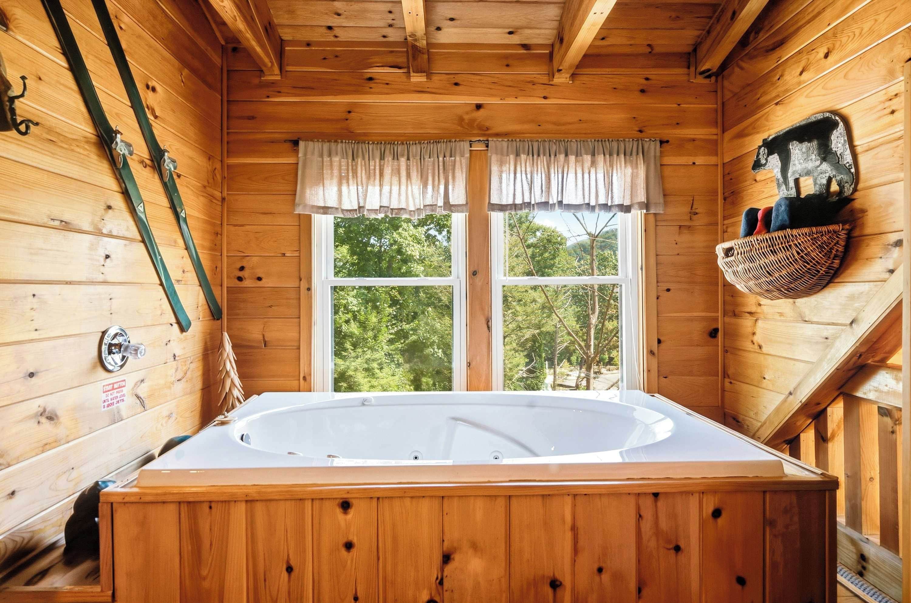 A wooden cabin with a large wooden bathtub, a window with curtains, and a basket on the wall.