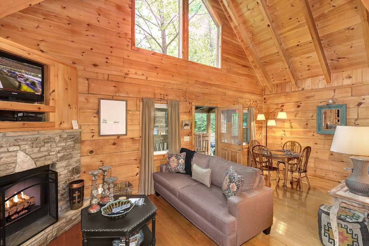 Un intérieur de chalet chaleureux avec une cheminée, un canapé, un coin repas et un téléviseur.