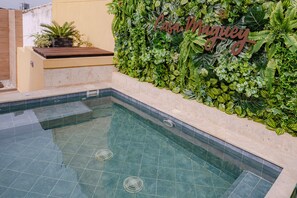 Una piscina con suelo de baldosas y una pared decorada con follaje verde y un letrero que dice "Casa Maguey".