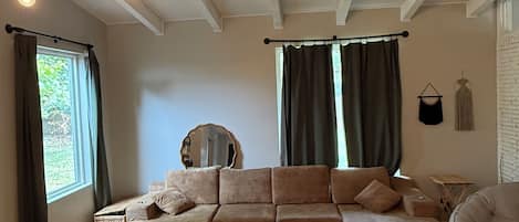 A living room with a sofa set, a round coffee table, a patterned rug, a hanging light fixture, and a window with curtains.
