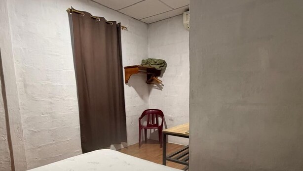 Una habitación con una cama, una silla, una mesita pequeña y un estante con una toalla.
