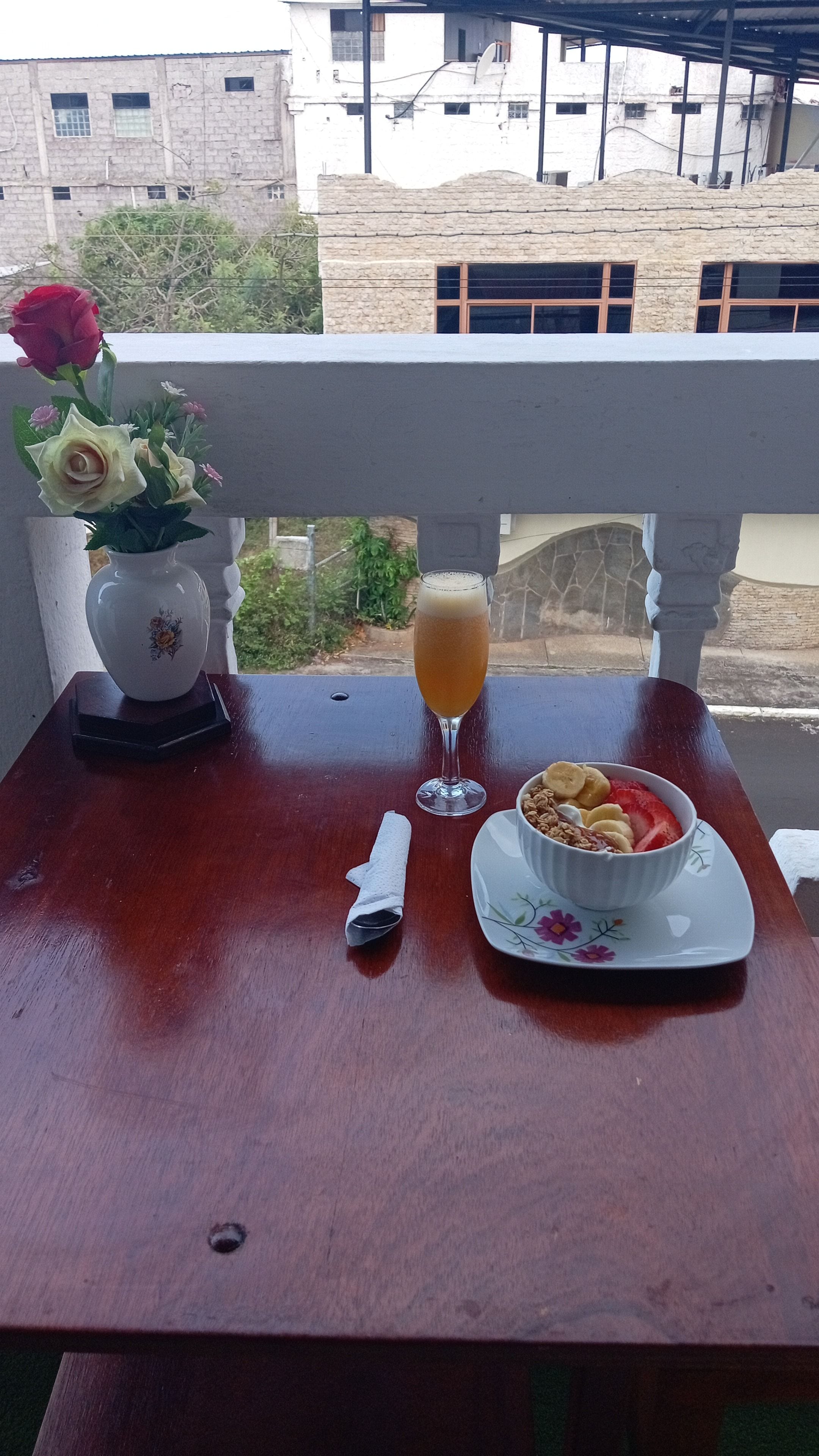 Een tafel met een kom ontbijtgranen, een glas sap en een vaas met bloemen.