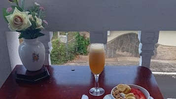 Een tafel met een kom ontbijtgranen, een glas sap en een vaas met bloemen.