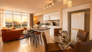 A modern apartment with a dining area, kitchen, and a large window offering a city view.