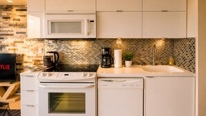 Una cocina moderna con microondas, estufa y lavavajillas, un salpicadero con diseño de ladrillo y un televisor de pantalla plana mostrando 'FLIX'.