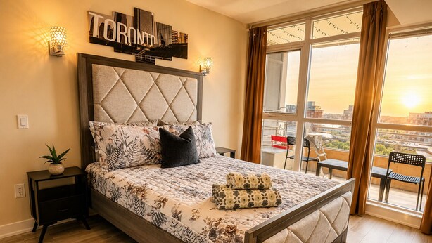 Un dormitorio con cama, mesita de noche, planta en maceta, vista a la ciudad y un cartel con la palabra 'TORONTO' en la pared.