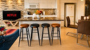 A modern kitchen with a built-in microwave, a coffee maker, and a vase with flowers. There are four stools and a dining table with chairs.