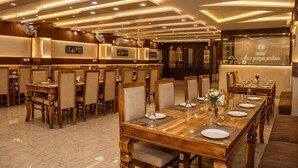 Comedor de hotel con varias mesas dispuestas para los huéspedes, con mobiliario de madera y un diseño de techo moderno.