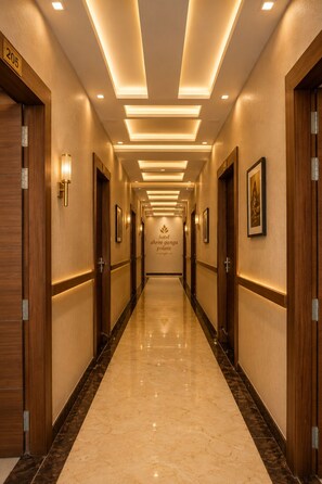 Corredor de hotel com piso de mármore, portas de madeira e luminárias fixadas na parede.