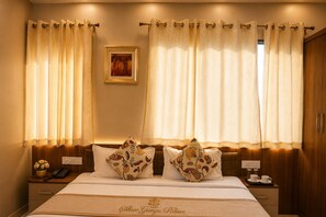 A hotel room with a bed, two decorative pillows, a bedside table with a phone and a vase, and curtains.
