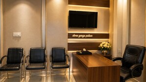 Un salón de conferencias con una mesa larga, tres sillas, un televisor y un cartel que dice 'Shree Ganga Palace'.