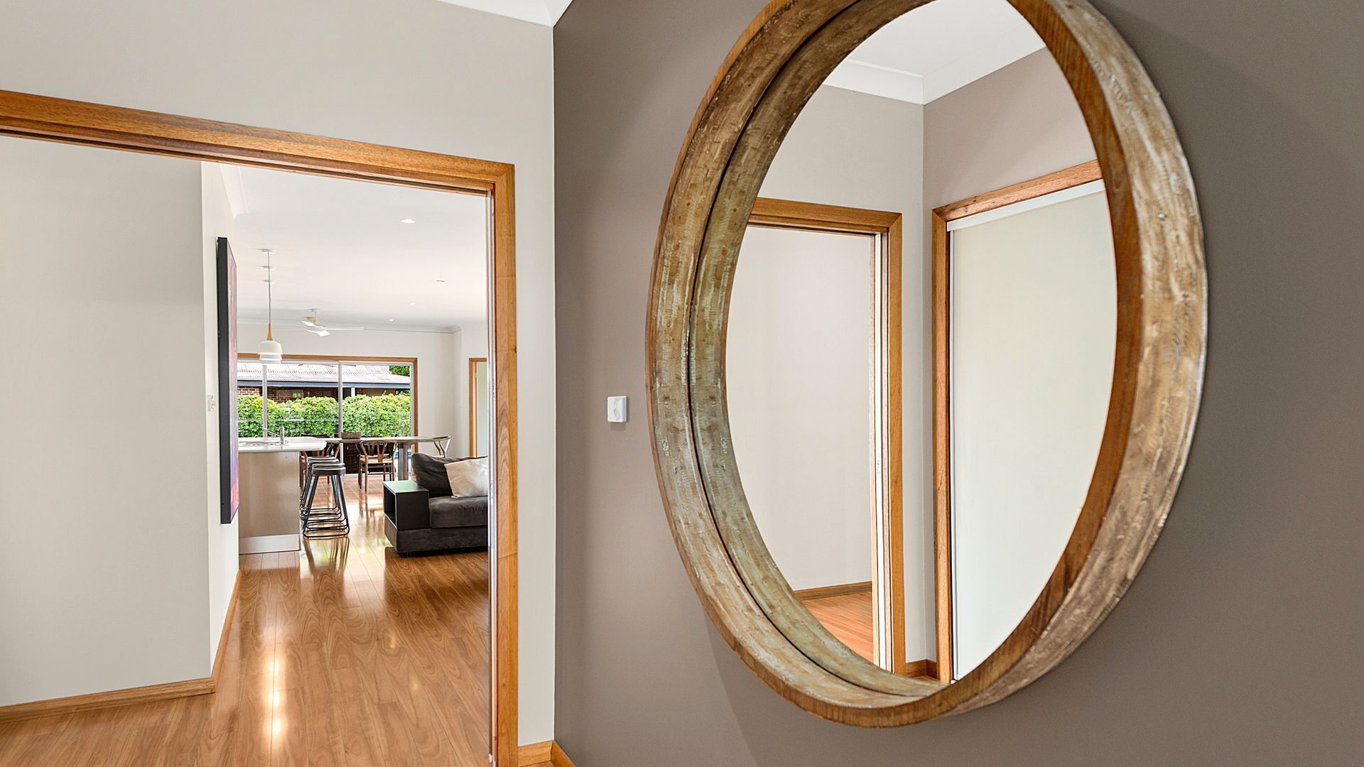 A hallway with a wooden-framed mirror and a view into a dining area with a table and chairs.