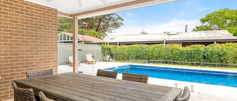 Une terrasse extérieure avec une piscine, une table et des chaises, et une vue sur un quartier résidentiel.