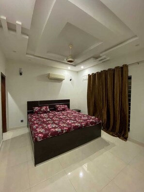 A bedroom with a bed, a ceiling fan, an air conditioning unit, and a window with curtains.