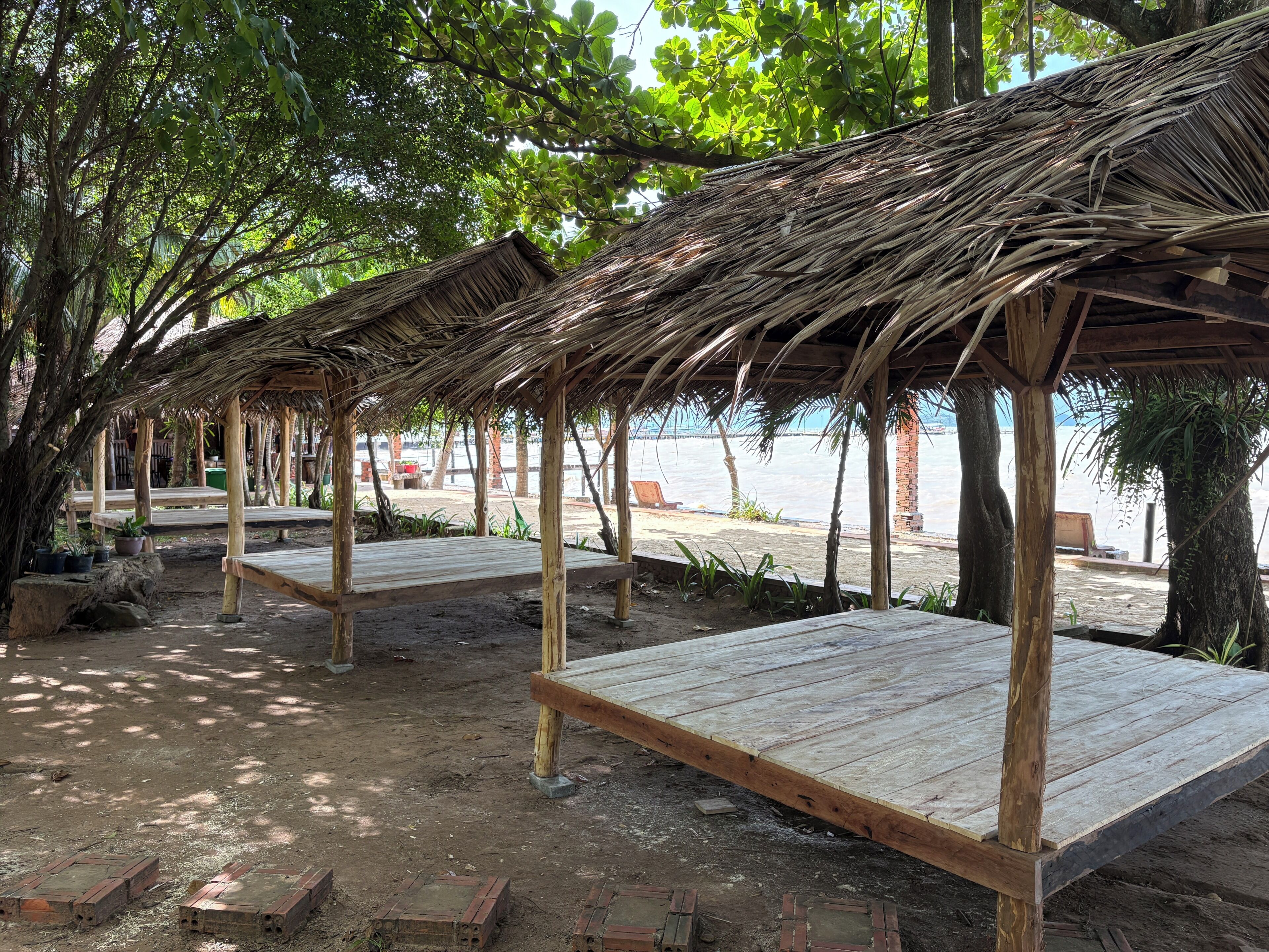 Una estructura frente al mar con bancos de madera y techo de paja, rodeada de árboles y vistas al mar.