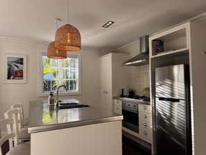 A kitchen with a central island, stainless steel appliances, a hanging light fixture, and a window with blinds. - Crab Shack Cottage: 4BR in Russell with Pool & Spa, 300m to Waterfront (Russell)