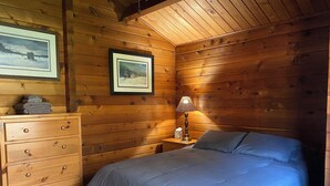 Une pièce de style cabane en bois, avec un lit, une commode et deux tableaux encadrés accrochés au mur.
