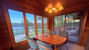 Un intérieur en bois avec une table à manger, des chaises et de grandes fenêtres donnant sur un lac.