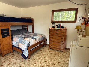 Un dormitorio con una cama litera, un aparador, una lámpara y una ventana.