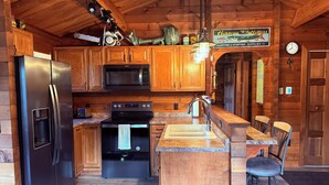 Ein Holzblockhaus-Interieur mit einer Küche, die einen Kühlschrank, eine Mikrowelle, einen Herd und ein Spülbecken beinhaltet.