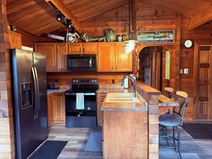 Interior de una cabaña de madera con cocina, que incluye un refrigerador, microondas, estufa y pileta.