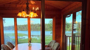 Ein Holzinterieur mit einem runden Tisch und Stühlen, großen Fenstern und Blick auf einen See.