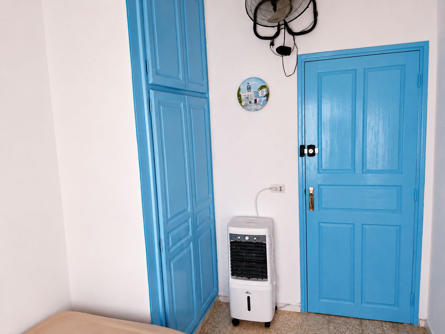 A room with a blue door, a white air conditioner, and a wall-mounted fan.