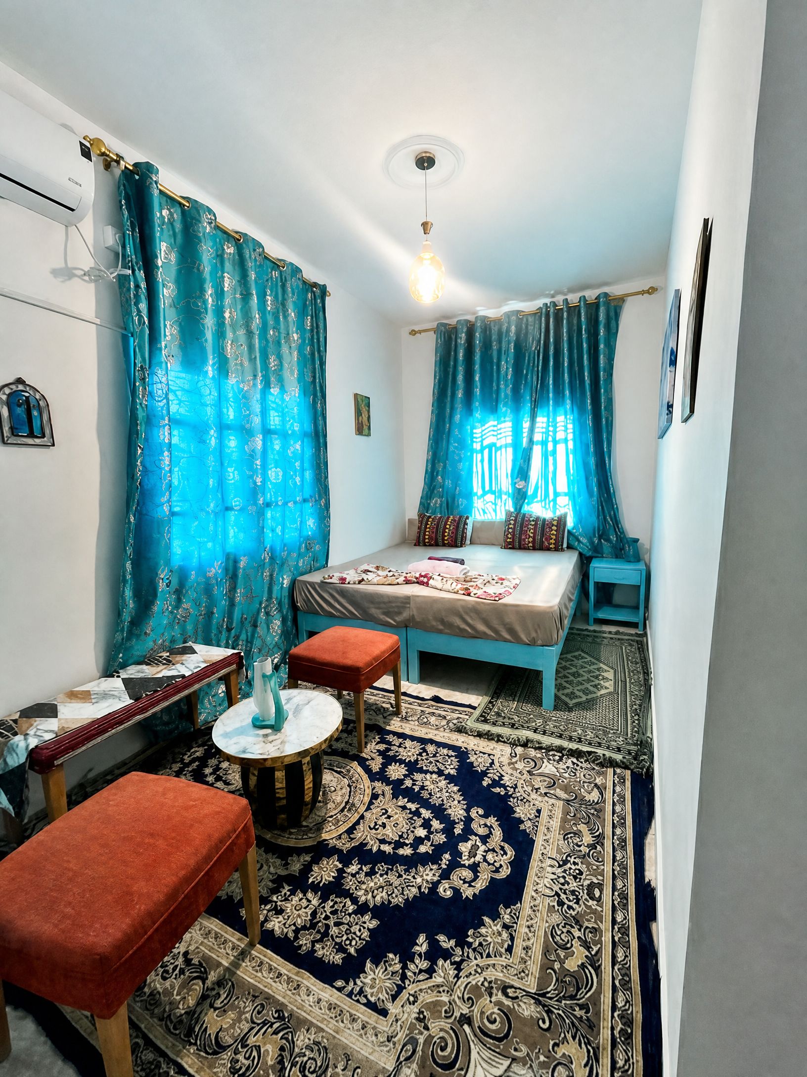 Un dormitorio con cama, una mesita, dos sillas, alfombra y cortinas.