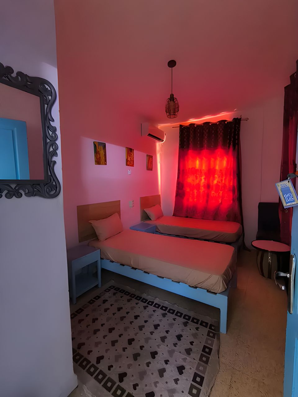 Ein Schlafzimmer mit zwei Betten, einem Spiegel, einem roten Vorhang und einem kleinen Tisch.
