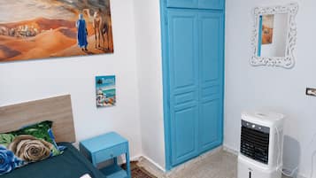 Un dormitorio con una cama, una mesita de noche azul, un calentador de pared, un cuadro enmarcado y un cartel.