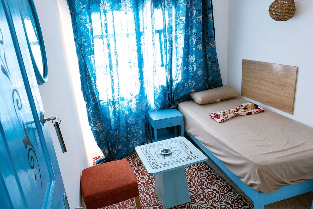 A room with a bed, a small table, a chair, and a door.