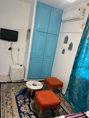 A room with a blue wardrobe, a television mounted on the wall, a small table with a decorative item, and a patterned rug. - Hotel Youssef Sousse Medina (Sousse)