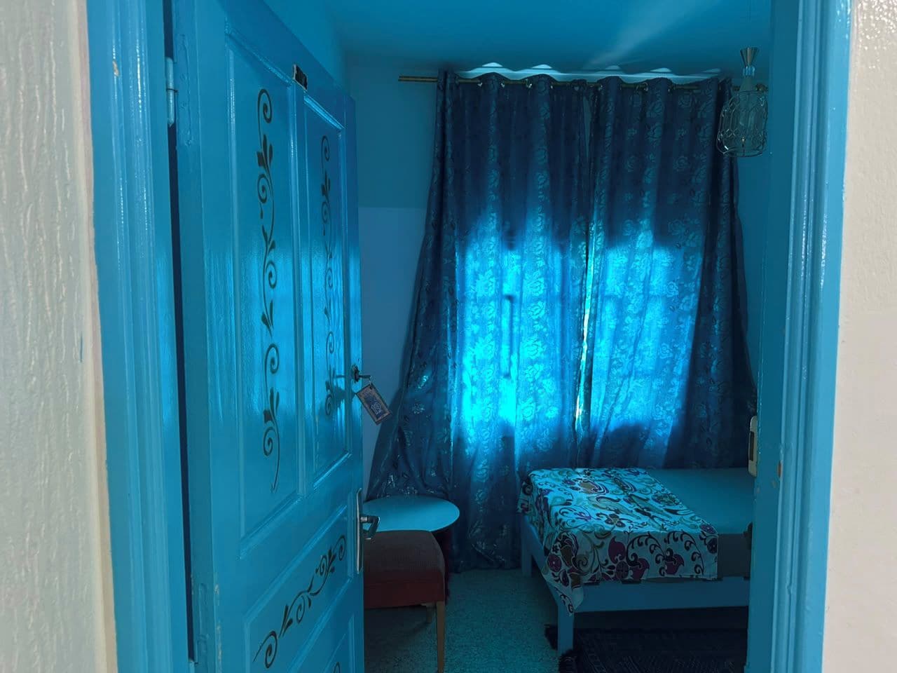 Une chambre à coucher avec un lit, une chaise, une petite table et une fenêtre avec des rideaux.
