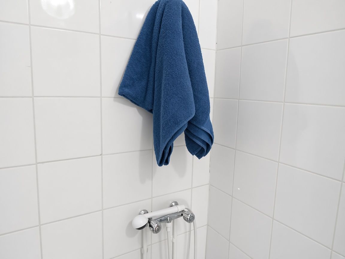 Ein Badezimmer mit weißen Fliesen, einem Handtuchhalter mit gefaltetem Handtuch und einer Duscharmatur.