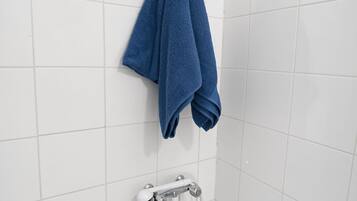 Ein Badezimmer mit weißen Fliesen, einem Handtuchhalter mit gefaltetem Handtuch und einer Duscharmatur.