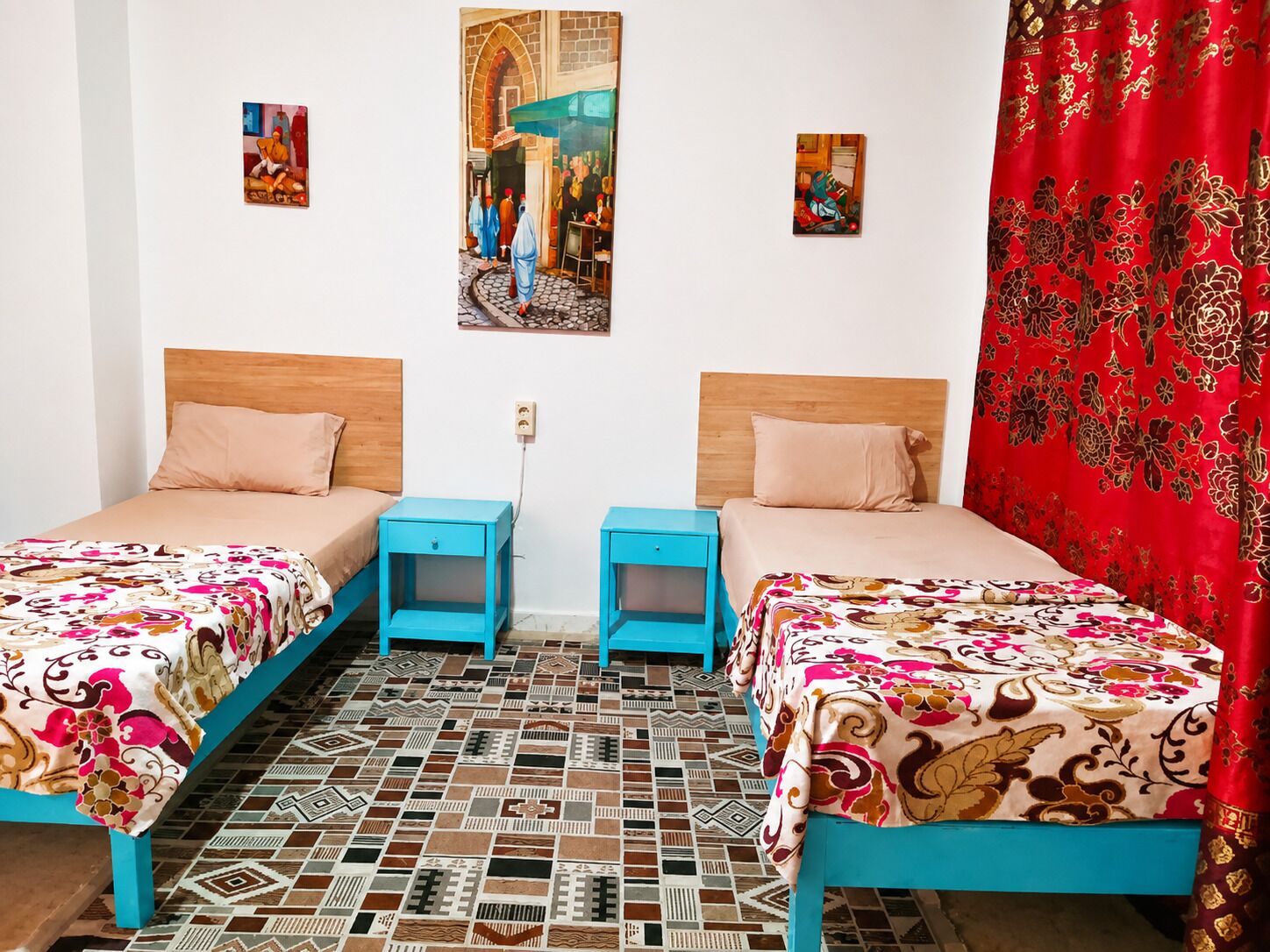 Une chambre avec deux lits, chacun recouvert d’une couvre-lit à motifs, une petite table et un tableau accroché au mur.