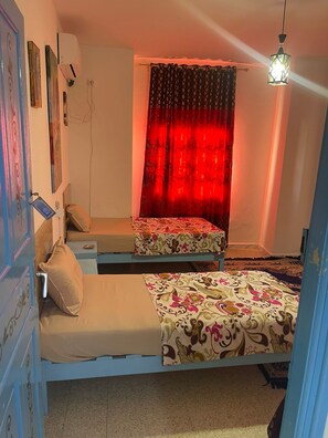 A room with two beds, a red curtain, a hanging light fixture, and a wall-mounted air conditioner. - Hotel Youssef Sousse Medina (Sousse)