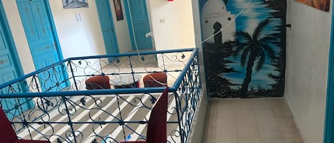 A hotel interior with a staircase, red chairs, a small table, and a mural of palm trees.