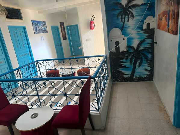 A hotel interior with a staircase, red chairs, a small table, and a mural of palm trees. - Hotel Youssef Sousse Medina (Sousse)