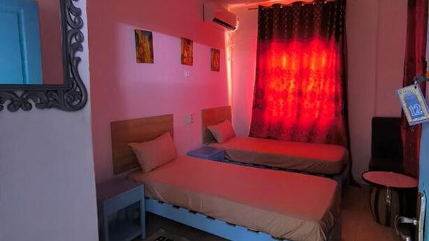 A bedroom with two beds, a mirror, a ceiling light, and a patterned rug.