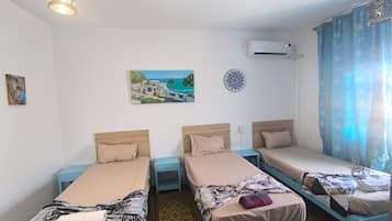 A room with three single beds, a ceiling light, an air conditioner, and a window with curtains.