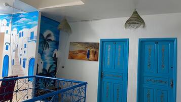 Une pièce avec une porte bleue, un tableau et un escalier dont les rampes sont bleues.